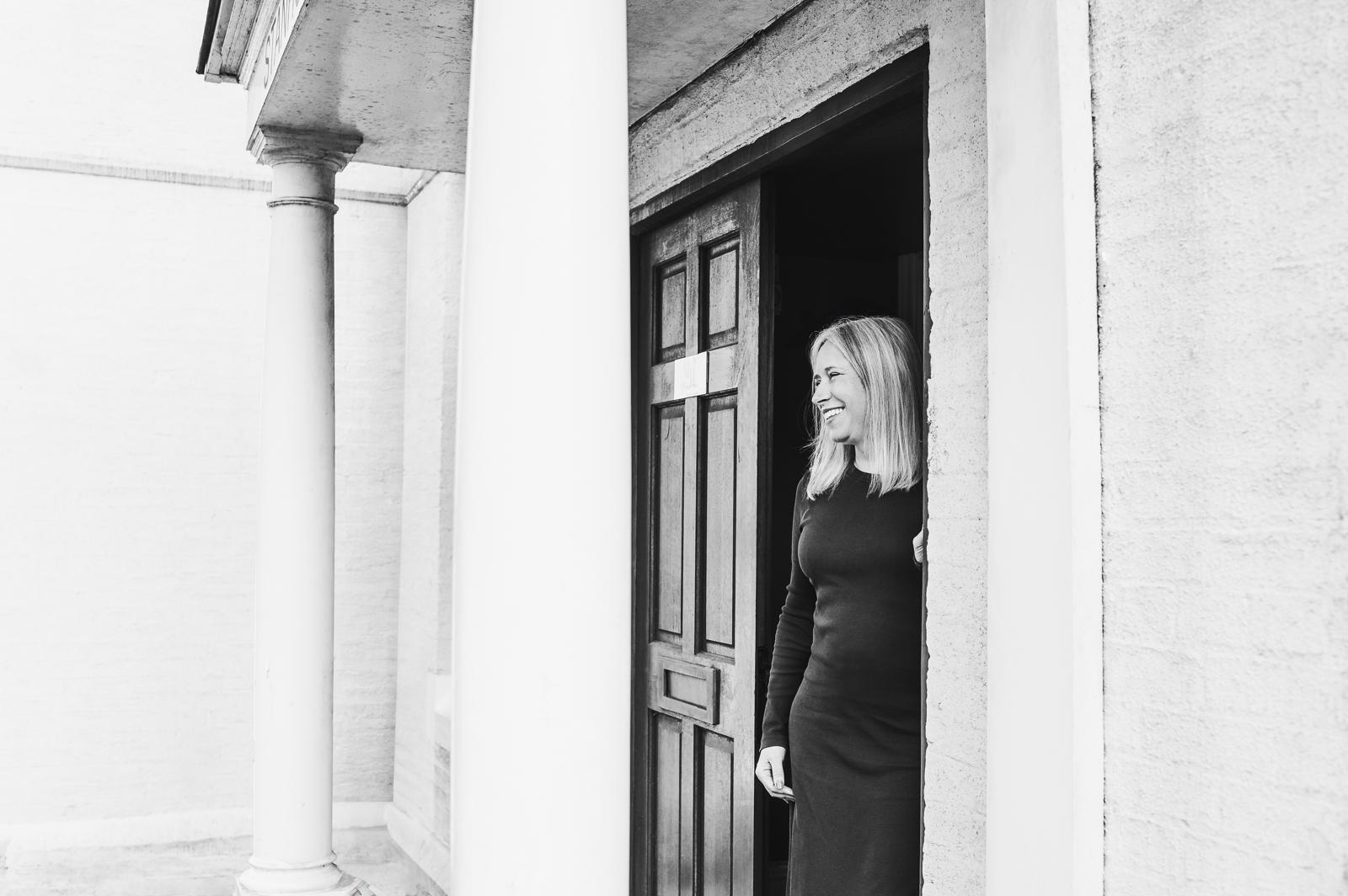 Black and white photo of Marie laughing in a doorway between stone columns