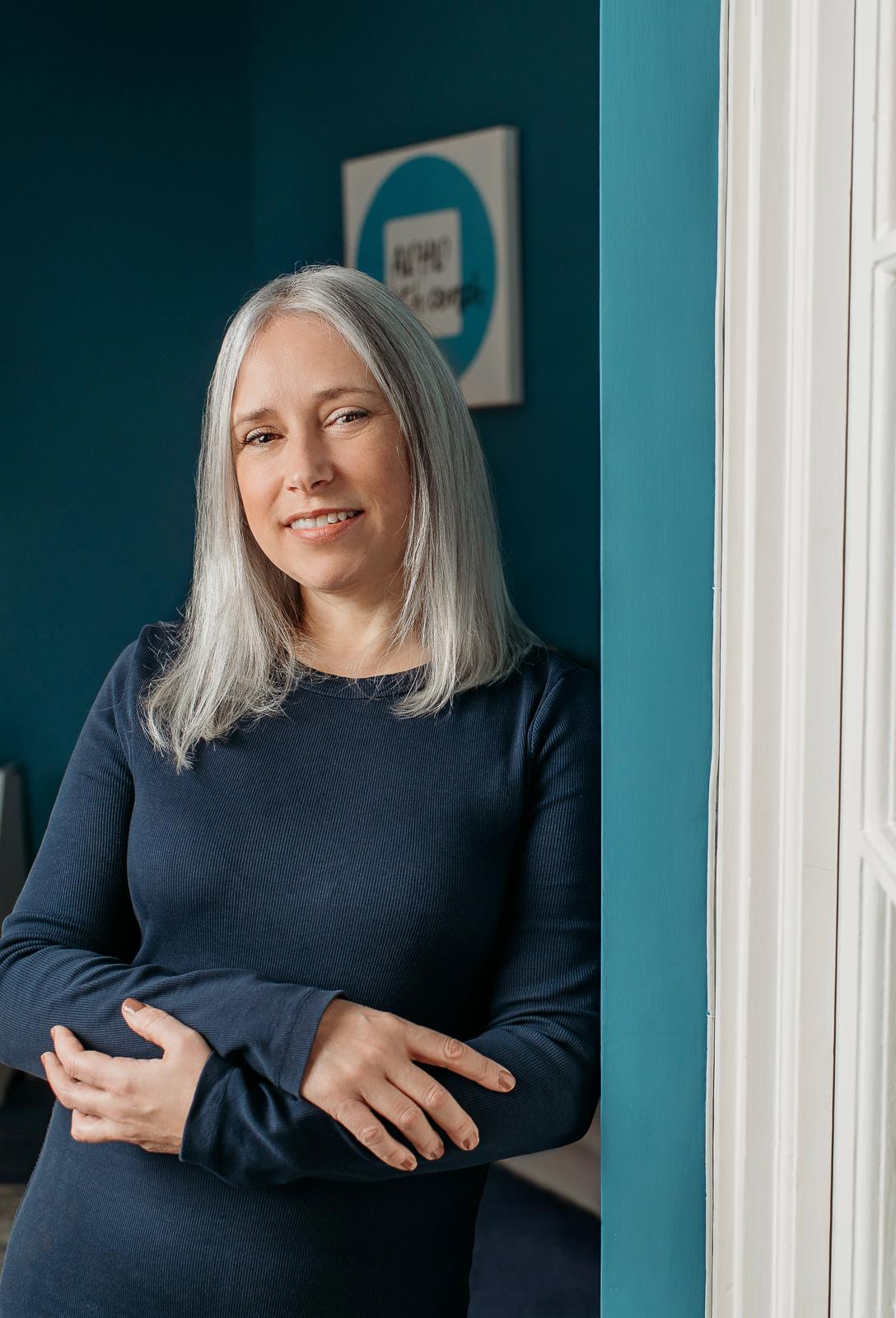 Marie smiling and leaning against a teal door frame with her arms folded