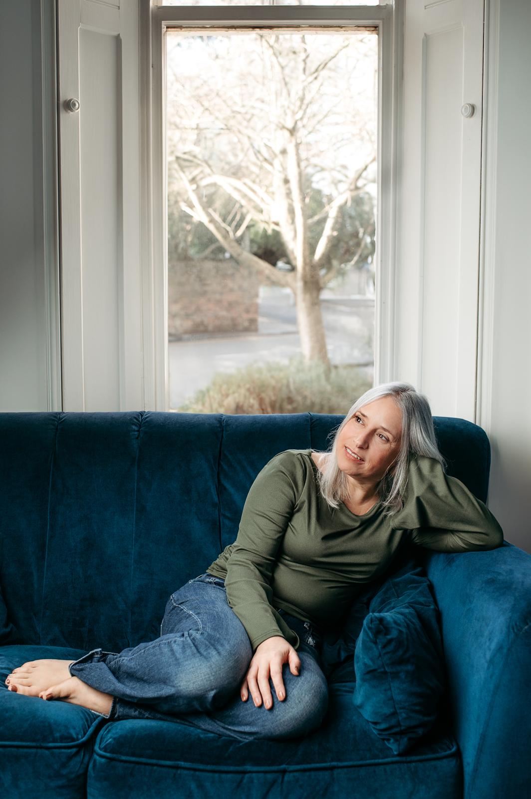 Marie relaxing on a blue velvet sofa by a tall window